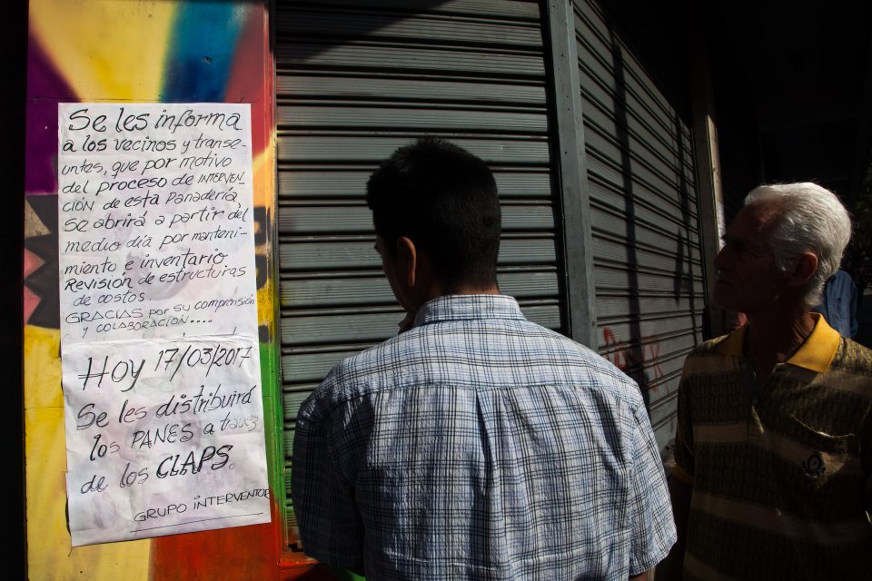People read a sign that reads, "Neighbors, for reasons of intervention this bakery will be opened after inspection and revision of its cost structure. Today, bread will be distributed through the Local Provision and Production Committees (CLAPS)," outside a bakery in Caracas, on Friday, March 17, 2017. Venezuelan bakeries are the latest industry to find themselves in the cross-hairs of President Nicolas Maduros administration as bread lines grow in the capital Caracas. The government has ordered bakers to use scarce supplies of flour to produce price-controlled loaves and said that only 10 percent can be used to make the unregulated, pricey treats loved by Venezuelans. Photographer: Wil Riera/Bloomberg via Getty Images