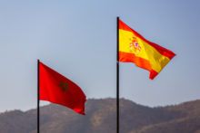 The national flag of morocco and spain waving in a blue sky