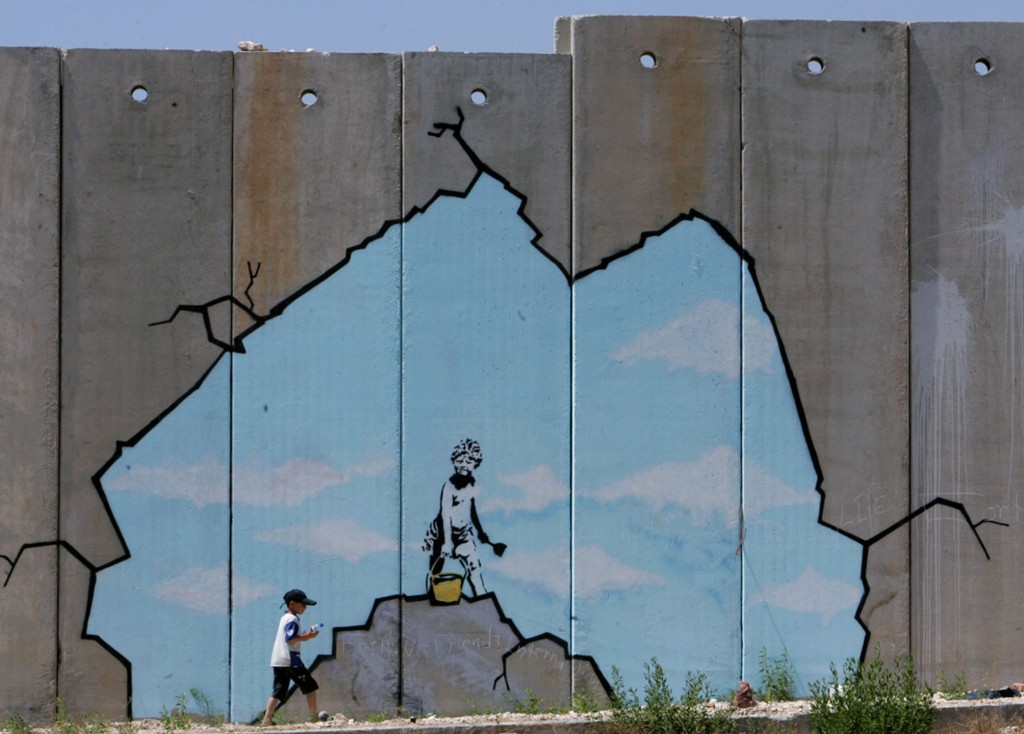 A Palestinian boy walks past a drawing by British graffiti artist Banksy near the Kalandia ...